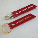 Deux porte-clés Atelier Guillocher en cuir rouge avec marquage personnalisé doré et argenté sur fond blanc